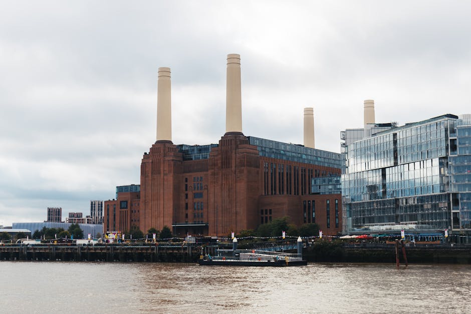 Black and white image of a railway yard with multiple train tracks curving toward a skyline featuring the Battersea Power Station with four tall chimneys, located in the background. The scene includes