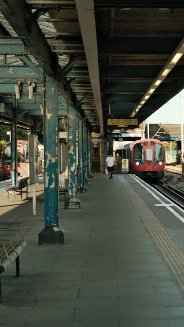 View of Clapham Junction station platform with a modern train featuring a silver body and red, blue, and white accents parked along the tracks. The platform surface is clean, with tactile paving visib